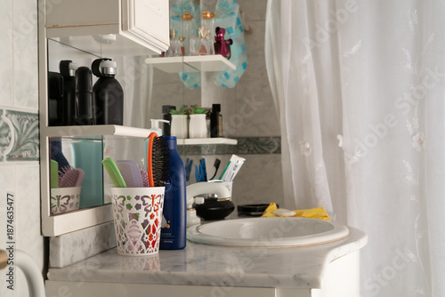 Container with brushes and combs, glass with toothpaste and toothbrush, soap and decorations on the countertop of a vanity in a bathroom.