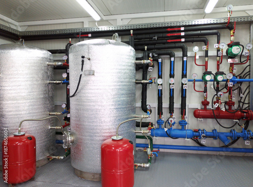 The interior of a modern gas boiler room. Visible are the pipes for supplying cold and hot water, large tanks, and numerous valves for shutting off the gas and liquid supply.