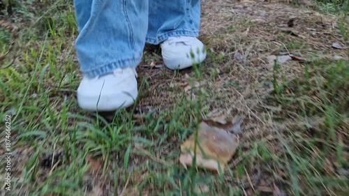 Walking in the forest. Feet in white sneakers, ground level view. Walking in the park or forest. Close-up of feet. Hiking outdoors in the summer