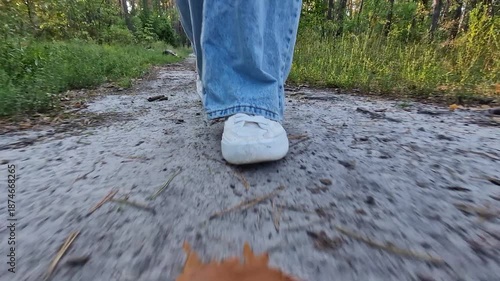 Walking in the forest. Feet in white sneakers, ground level view. Walking in the park or forest. Close-up of feet. Hiking outdoors in the summer