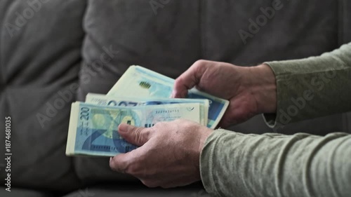 Male hands count Israeli new shekel banknotes in blue color with a 200 NIS denomination in a close-up view