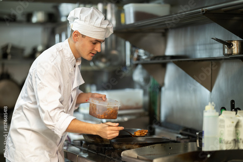 Foto Young man restaurant employee is busy preparing dish in kitchen