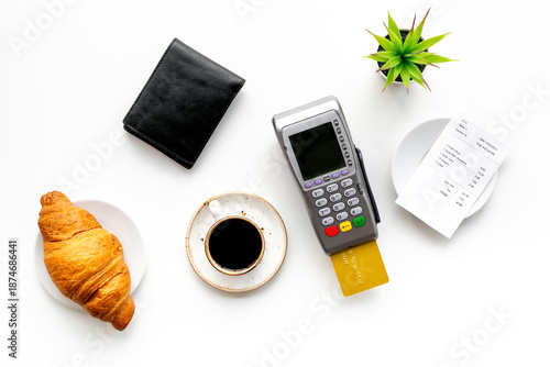 Paying the bill by pos terminal in cafe or restaurant. Cup of black coffee and croissant, payment wireless machine and bill on white background, top view