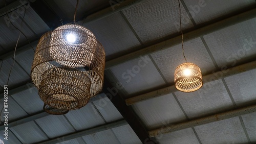 Two woven rattan pendant lamps hanging from a metal ceiling with exposed beams in a warehouse or industrial setting.