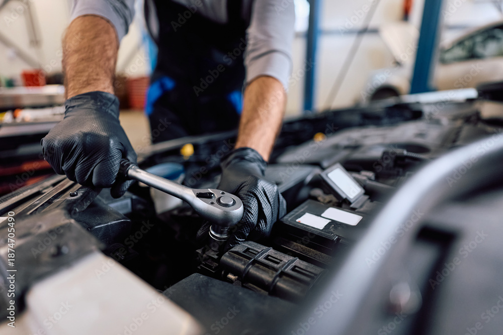 Fototapeta premium Close up of mechanic using wrench while working on car engine in workshop.