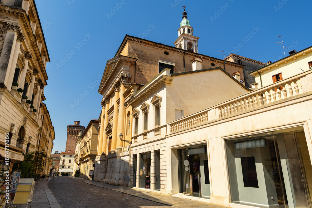 Fototapeta premium Narrow tunnel street in Vicenza, northeast Italy. Immutable row of buildings on both sides of street forms narrow passage, paved pavement of ancient city..