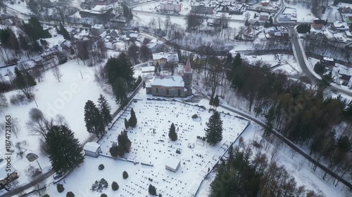 Experience the serene beauty of the Church of St. Peter and Paul in Tanvald, surrounded by winter's snow-covered landscape. Aerial views showcase the peaceful scene.