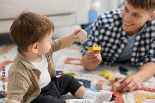 Bild auf Leinwand Smiling male nanny and cute little boy playing with toys on floor at home, selec