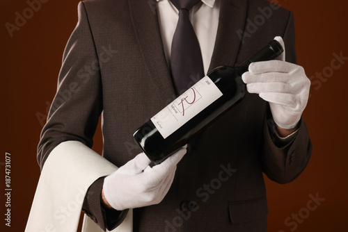Canvas Print Professional sommelier with bottle of red wine and napkin on brown background, c