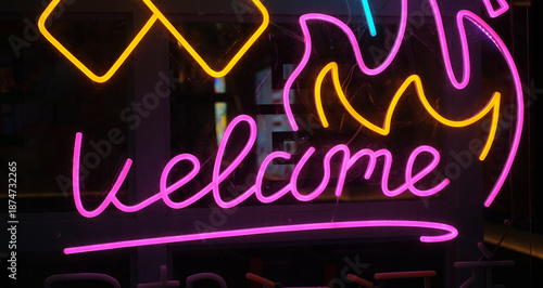 A glowing neon light sign mounted on a dark window, featuring the word Welcome in bright pink cursive typography