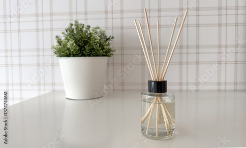 A minimalist home decor composition featuring a clear glass reed diffuser bottle with wooden sticks standing on a glossy white table