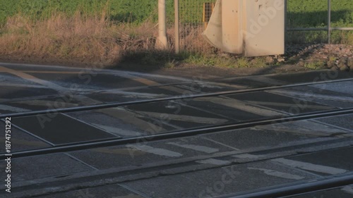 small silver hatchback car drives over railroad crossing aka railway level crossing, close up wheels, UK drives on left side of road, sync audio sound