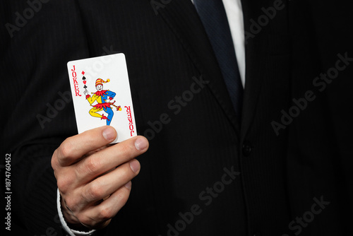 Tableau sur toile Close up to a businessman on suit holding a joker card on his hand at the left s