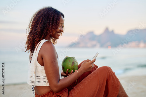 Photos Woman relaxing on a beach lounge with fresh coconut water and using a smartphone