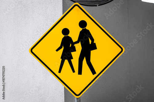 Fotografi Yellow sign warning of a pedestrian crossing mounted on a concrete wall