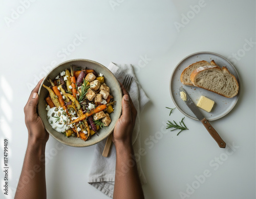 Vista superior de manos sosteniendo un tazón de comida saludable con pollo asado, zanahorias, queso feta y salsa de yogurt al romero.