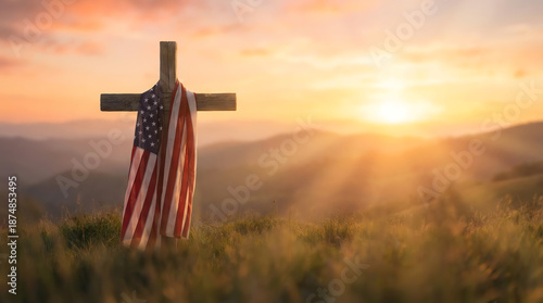 Wooden cross draped with an American flag stands in a grassy field at sunset, symbolizing patriotism and faith against a backdrop of mountains and warm glowing light