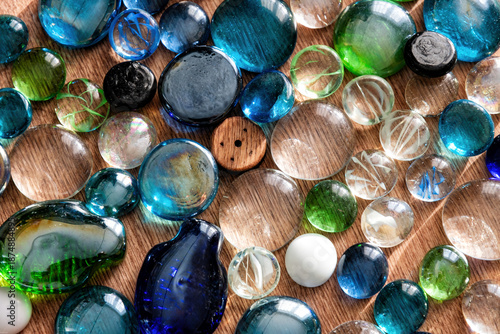 Vibrant glass pebbles and marbles, reflecting light in shades of blue, green, and clear, form a serene, textured background on wood