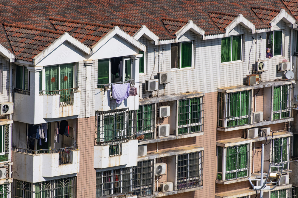 Obraz premium An older residential apartment building with window grilles, hanging laundry in Liuzhou, China. Dense urban housing reflecting everyday living conditions in a high-density neighborhood in Asia.