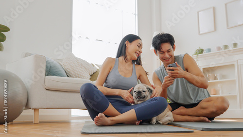 Asian couple with a male man and female woman relax during home exercise, using a smartphone with their dog and pet nearby.