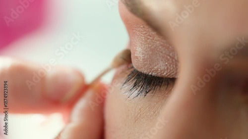 Extreme closeup of a makeup artist applying soft shimmer eyeshadow on a closed eyelid with a detail brush in a beauty salon. Clean background, long lashes, natural tones, professional hygiene