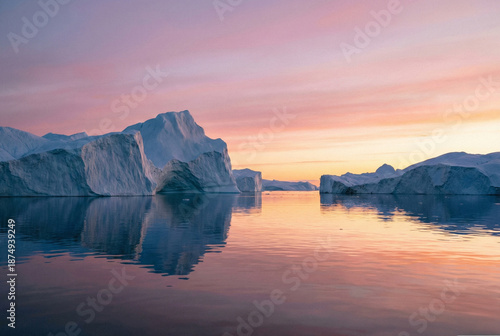 Large icebergs floating in Disko Bay illuminated by the colorful pink and orange light of the Arctic midnight sun