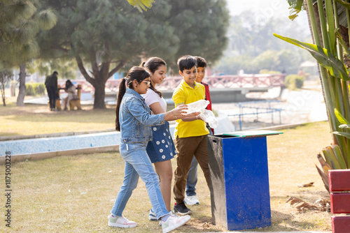 Young indian children throw plastic bottles into a trash. Garbage recycling bin in summer park, concept of teamwork, Waste reduction sustainability and community responsibility. Childhood activity.