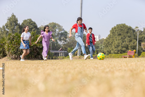 Φωτογραφία Group of indian children playing soccer or foot ball in summer park, Playful asian kids enjoying fun outdoor sports activity