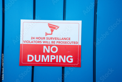 Fotografie No dumping sign with 24 hour surveillance warning attached to a blue corrugated