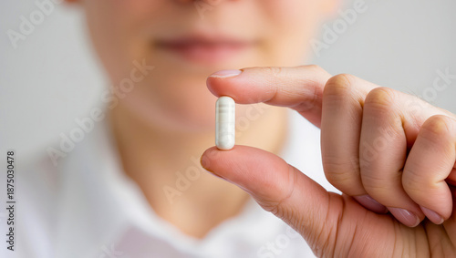 Close up of a persons hand holding a single white capsule pill.