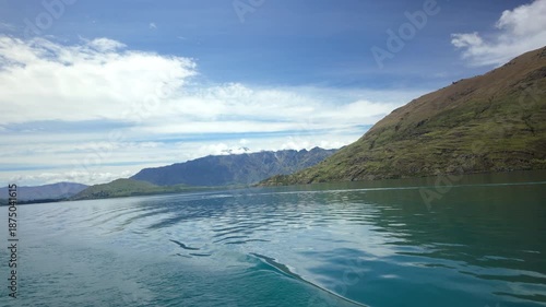Boat wake on calm lake with misty mountains and blue sky