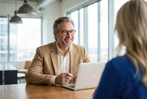 Wallpaper Mural Businessman in a beige suit smiles while engaging in a conversation with a woman at a modern office desk, showcasing a collaborative work environment with natural light Torontodigital.ca