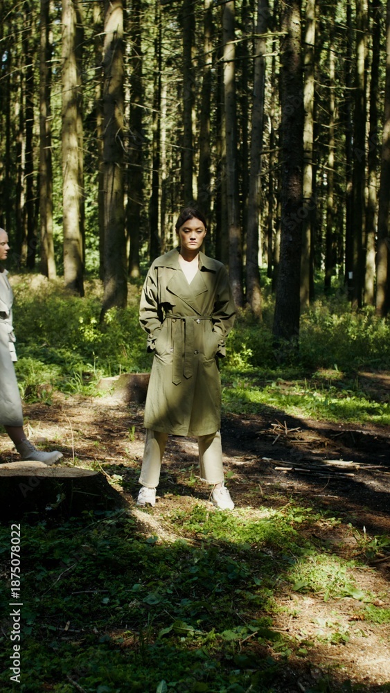 Fototapeta premium Two women walk past a standing model, in the forest, vertical video
