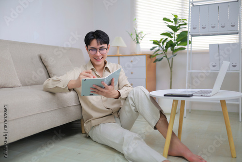 Happy young man casually writing notes in a personal organizer, planning and working remotely from his comfortable living room