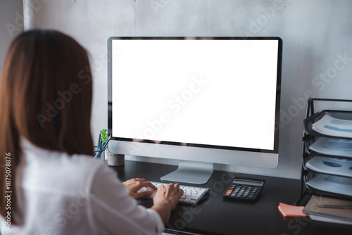 Woman typing on blank screen computer creating a mockup display for website, app, or software promotion at office desk