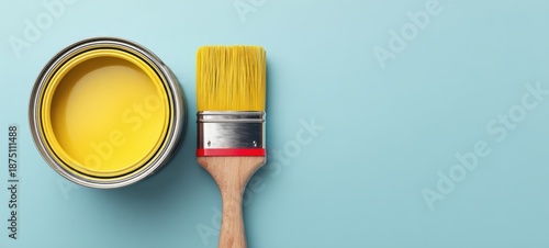 The paint can and brush with yellow paint on pastel blue background for decorating