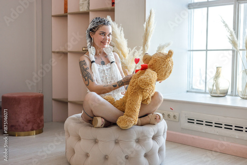 Portrait of beautiful dark-haired woman in pajamas posing with teddy bear in room