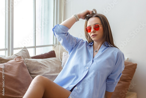 Portrait of a beautiful dark-haired woman in a blue shirt posing on her bed at home.