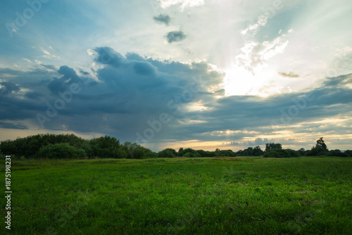 The sun emerges from behind a cloud over a green meadow