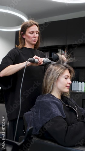 Professional female hairdresser blow drying and styling bob haircut for woman client wearing black clothes, indoors inside modern beauty salon, natural light, contemporary interior