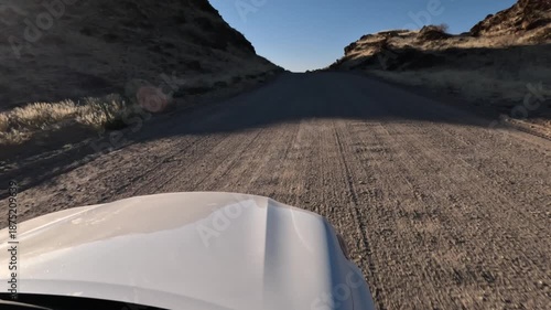 A lone white car drives along a dusty dirt road in southern Namibia, Africa.