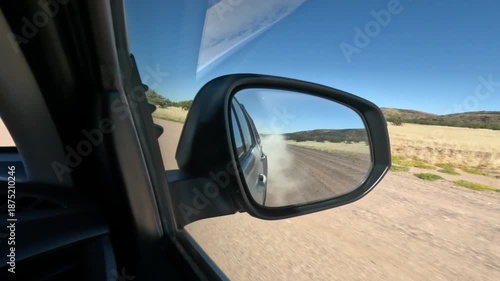 View in rear view mirror while driving through arid dry dusty road landscape in  Namibia