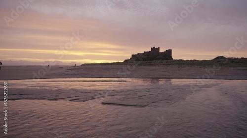 A low-angle static wide shot of the majestic Bamburgh Castle silhouetted against a golden sunrise sky