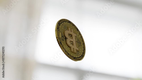 Close-up of a gold Bitcoin coin suspended in mid-air with a blurred white background.