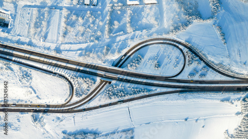 Aerial top-down view of a highway interchange and roads completely covered in white snow during winter.