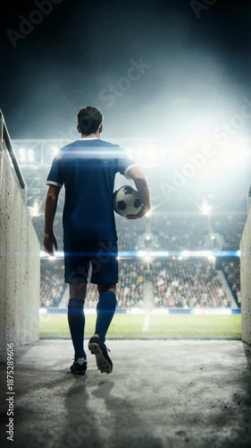 Silhouette of a soccer player holding a ball in a dark tunnel walking towards a bright stadium. Football athlete entering the arena pitch for a night match. Vertical video for social media