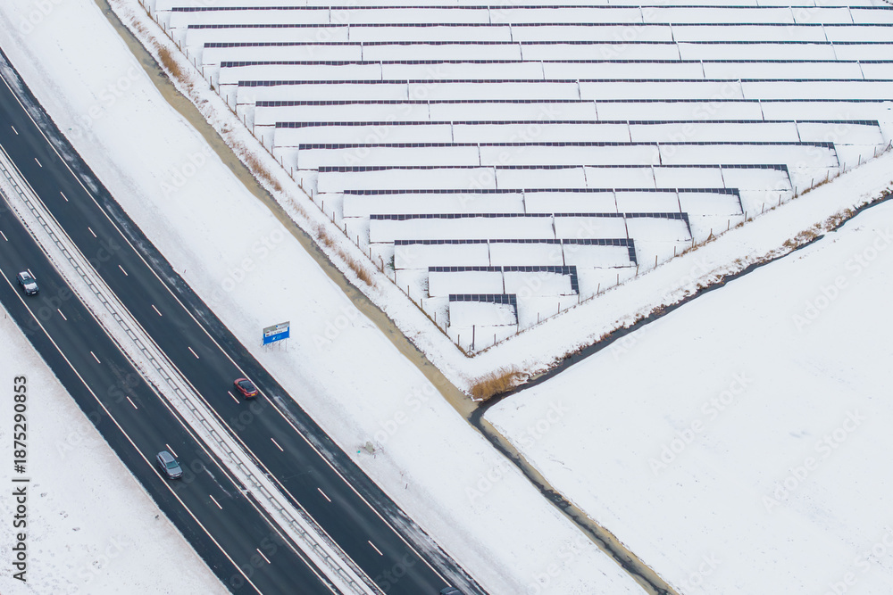 Fototapeta premium Aerial winter road alongside snow covered solar panels