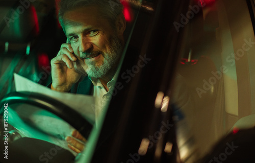 Mature businessman on phone reading document in car at night