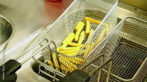 Chef shakes out oil from strainer with French fries over fryer closeup. Cooking tasty crispy snacks in fast food restaurant kitchen