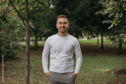 Portrait of a man against the backdrop of a green park. The young man is smiling and looking straight ahead.